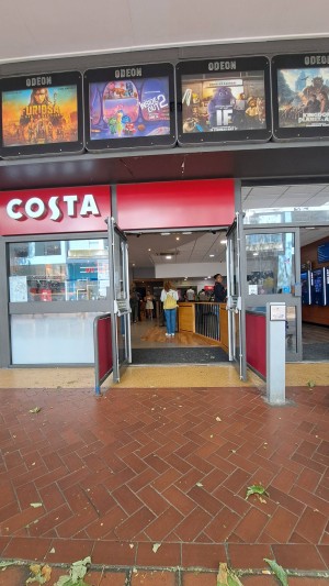 Double glass doors in black metal frame. Barriers to left and right as you approach. Push button at start of right barrier to open. Doors open out.
