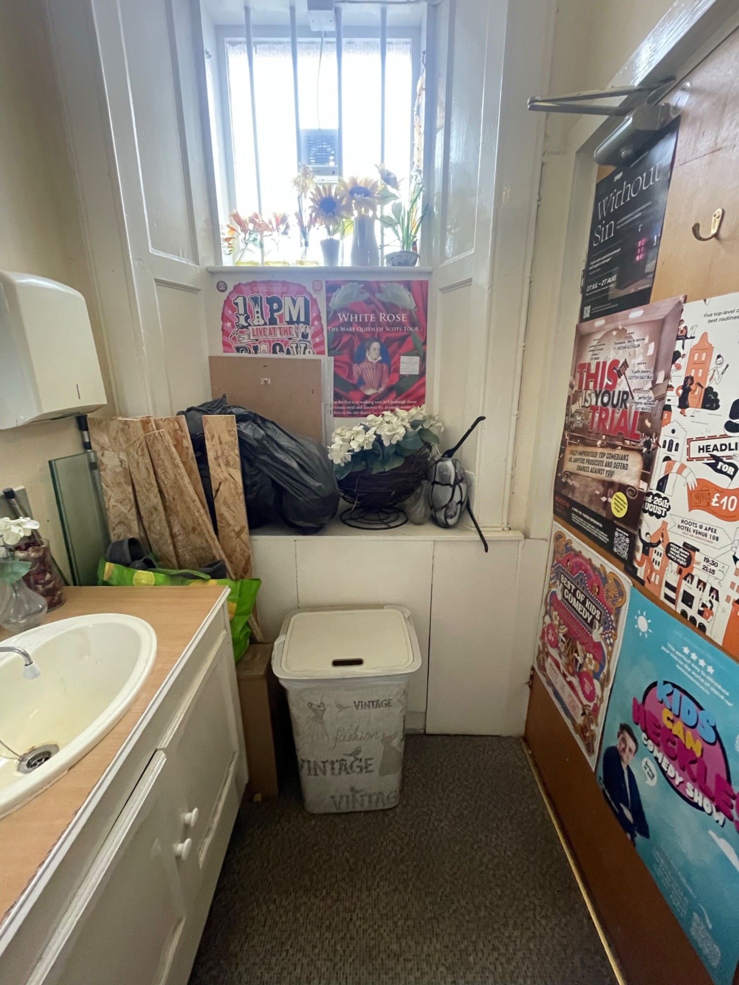 From door looking right. Sink on left. Stored items on back wall. Door on right. High hanging hook in centre of door.