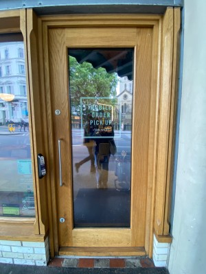 Glass door, with wooden doorframe. Handle on left. Push to open.