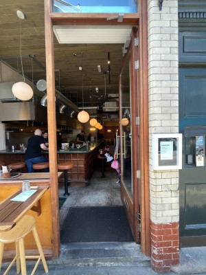 Glass door with brown wooden frame. Push open via long gold metal handle on left.