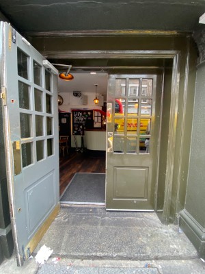 Glass double door, with wooden green doorframe. Gold metal handles at centre. Pull to open.