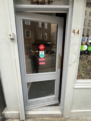 Glass door in grey wooden frame. Push silver metal panel from right to open.