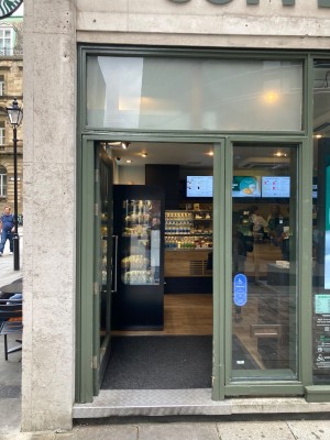 Glass door with green frame. Vertical metal handle on right side. Assistance touch button on the right side of the door.
