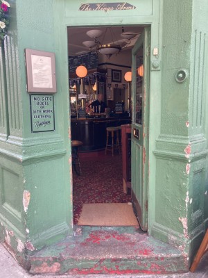 Green and glass panelled door with gold pad on right, push to open. Step up before door.