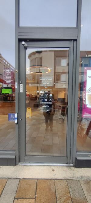 Grey metal framed glass door ahead. Pull handle on left to open. Doorbell for assistance to its left.