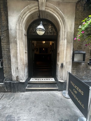 Black and glass panelled doors. Push silver pads in centre to open. Queue barrier to right of entrance.