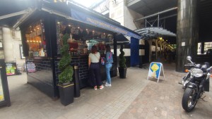 From sidewalk facing venue. Open counter along left. Path in centre. Pillars on back right.